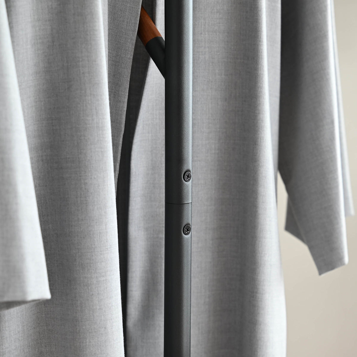 Close-up of the black Yamazaki Home Coat Rack (70" H) - Steel pole joint and two screw heads visible between the folds of a hanging grey coat.