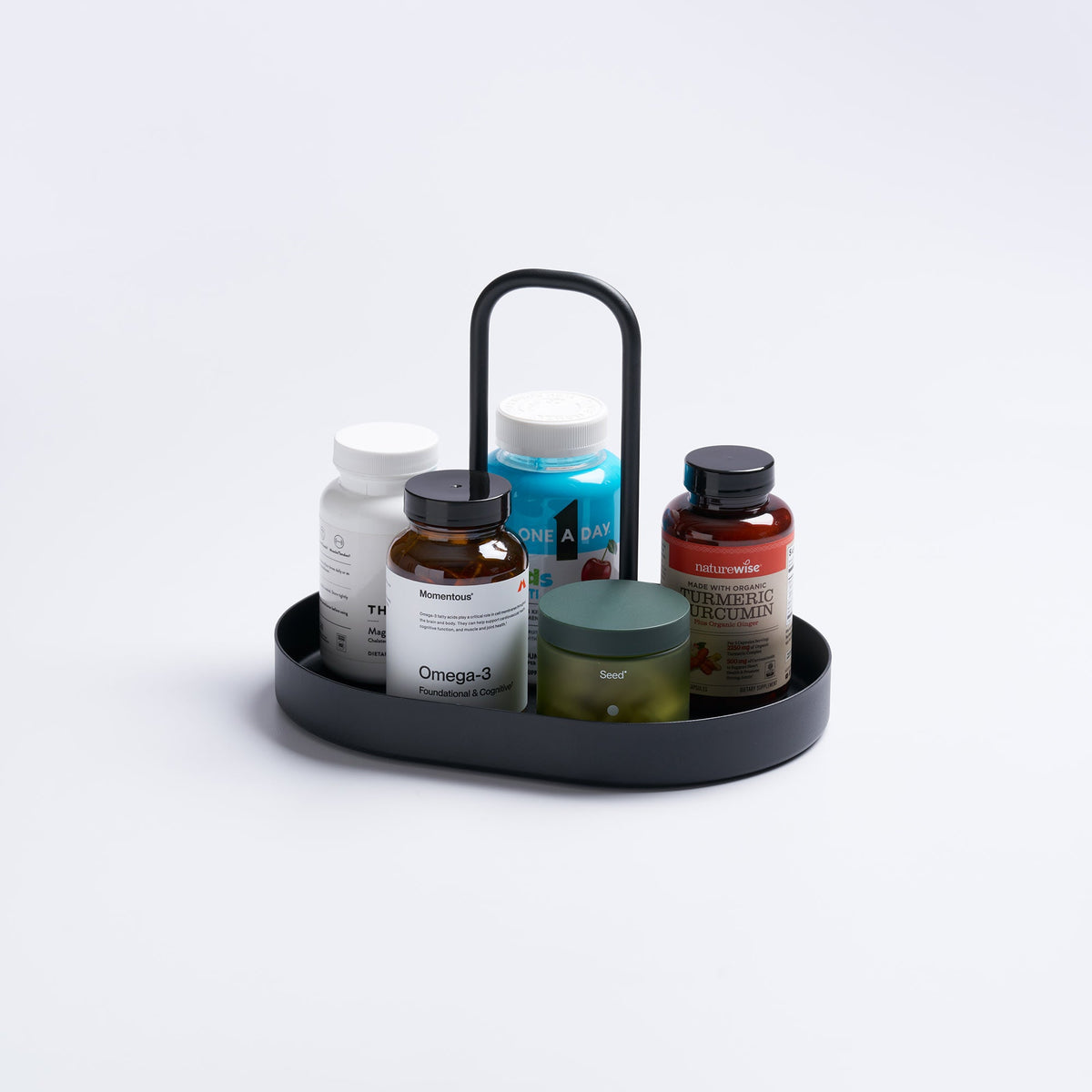 Black Yamazaki Home Vanity Tray with Handle - Steel holding assorted supplement bottles and a green jar, with the tall handle rising behind the containers.