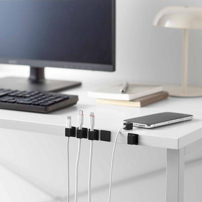 Black Yamazaki Home Magnetic Cable Holders With Adhesive Steel Bases (Set of 5) - Silicone arranged along a white workstation, keeping charging connectors beside a phone beneath a monitor.