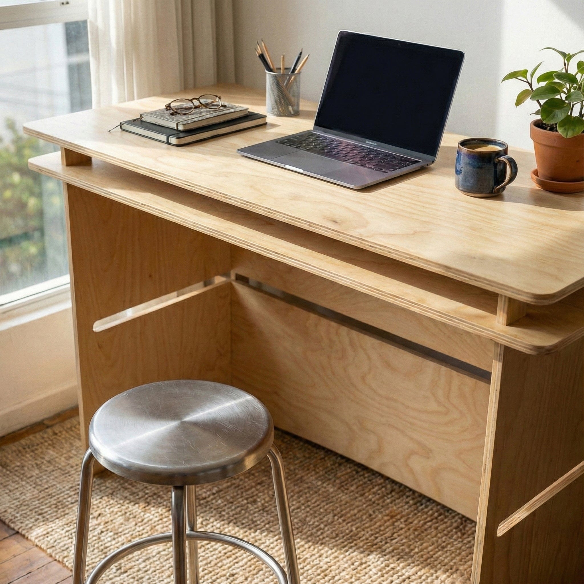 Close angled view of the Williamsburg desk holding a laptop, keyboard, pencil cup and mug, showing its raised upper shelf and spacious work surface