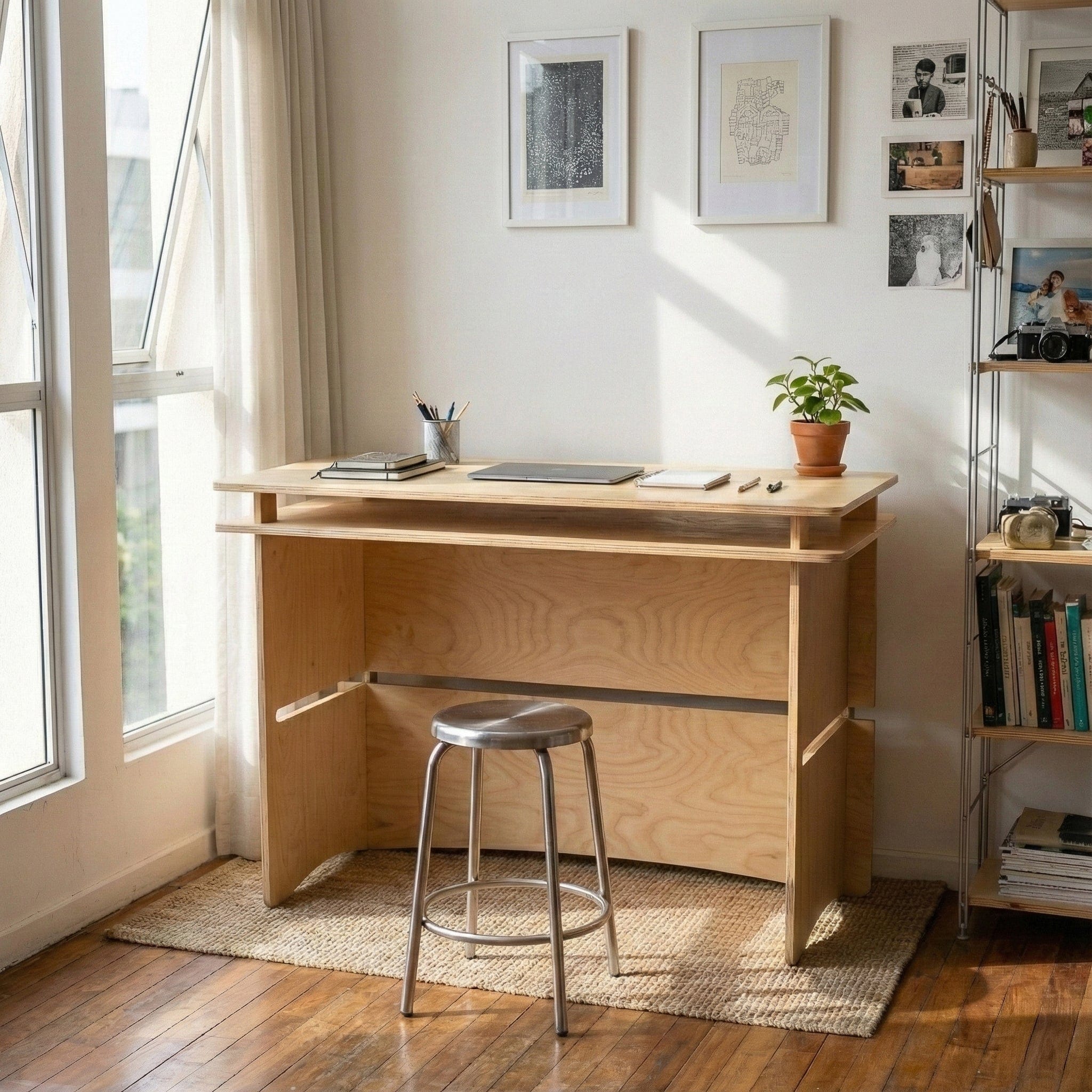 Williamsburg wood desk styled with notebooks and a small plant in a sunlit home office, paired with a round metal stool