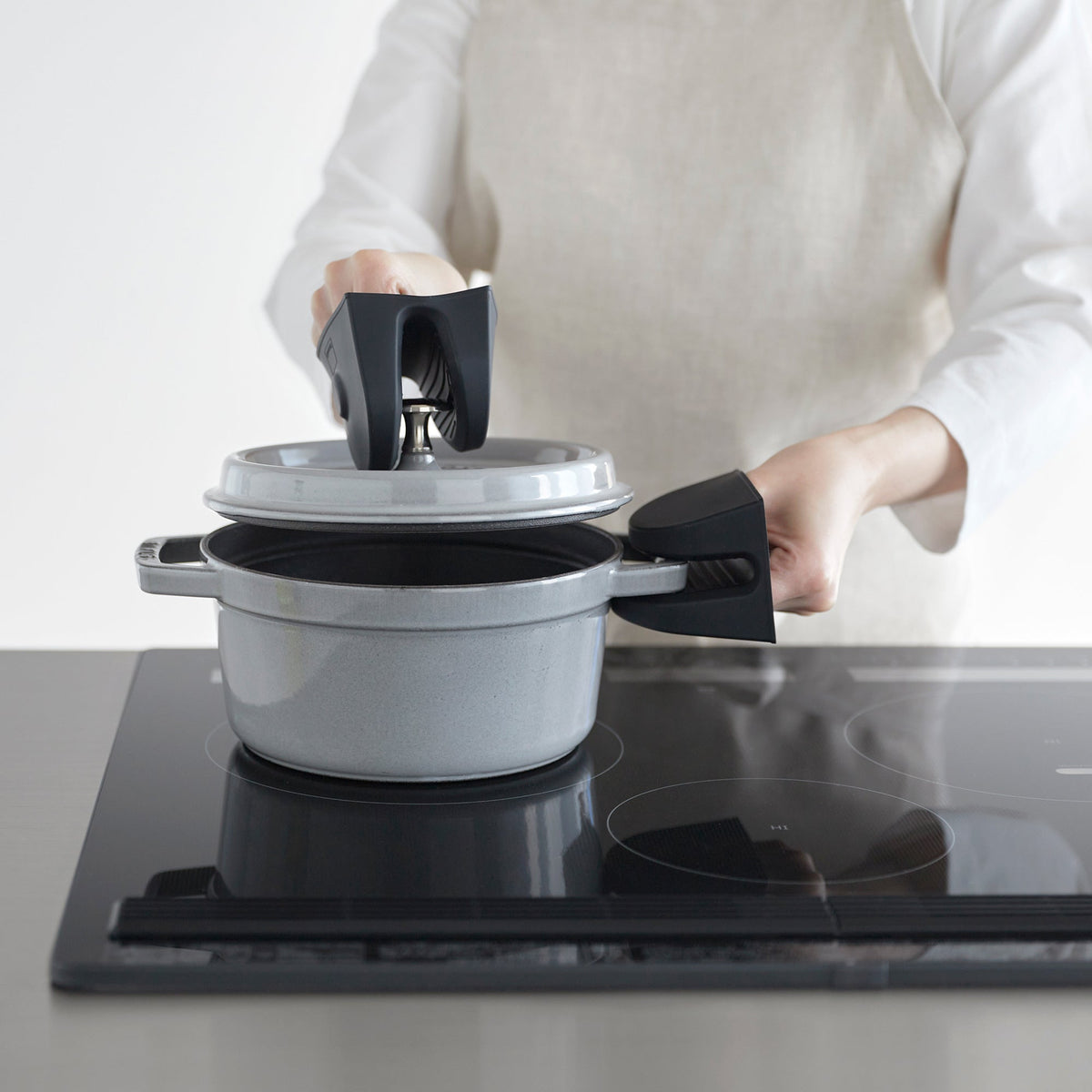 Black Yamazaki Home Magnetic Pot Holders - Set of 2 - Silicone used to raise a grey pot lid while holding the pot’s side handle over a glass cooktop.