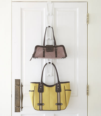 White Yamazaki Home Cascading Storage Hooks - Steel on a white panelled door, holding a small patterned handbag above a large yellow tote with dark handles.