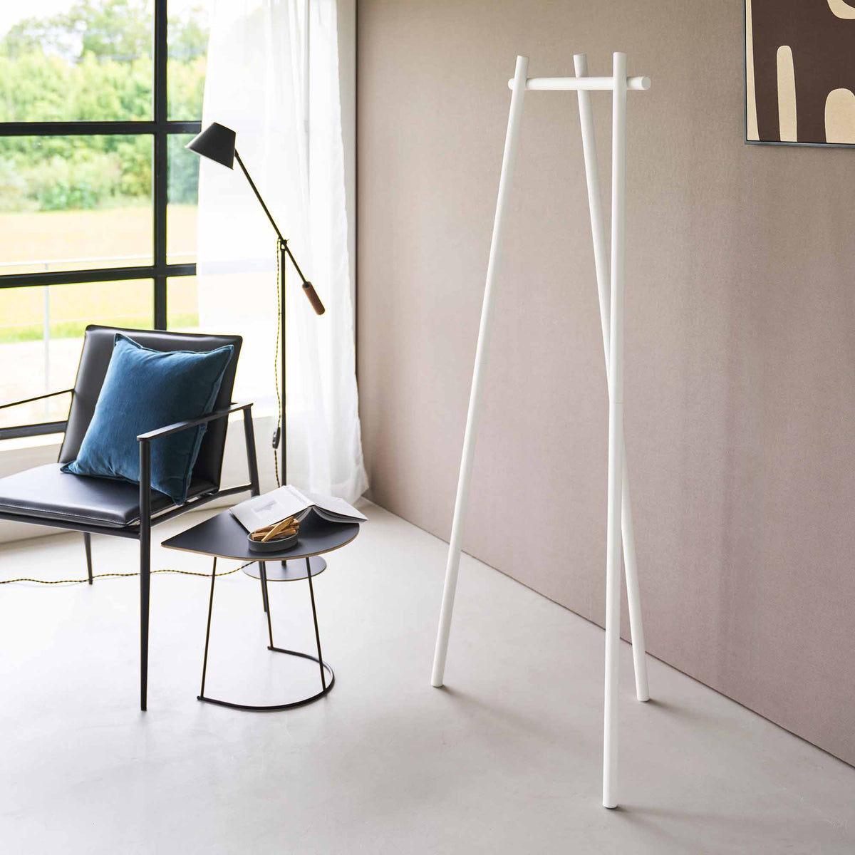 Empty white Yamazaki Home Tri-Post Coat Rack (60" H) - Steel beside a beige wall, showing its three tall posts, splayed feet and short horizontal rail near a window and lounge chair.