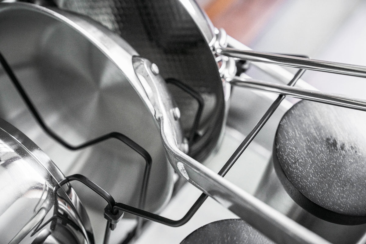 Glass-lid detail on the black Yamazaki Home Adjustable Pot Lid Organizer - Steel, with the black lid handle nestled into the curved dip of a wire divider.