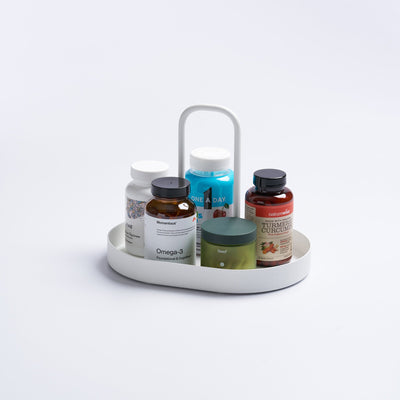 White Yamazaki Home Vanity Tray with Handle - Steel holding assorted supplement bottles and a green jar, with a shallow oval base, raised rim and tall rounded rectangular handle.
