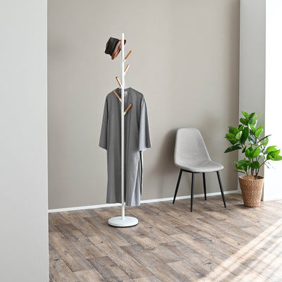 White Yamazaki Home Coat Rack (70" H) - Steel holding a long grey coat and dark hat in a room with wood flooring, a grey chair and a potted plant.