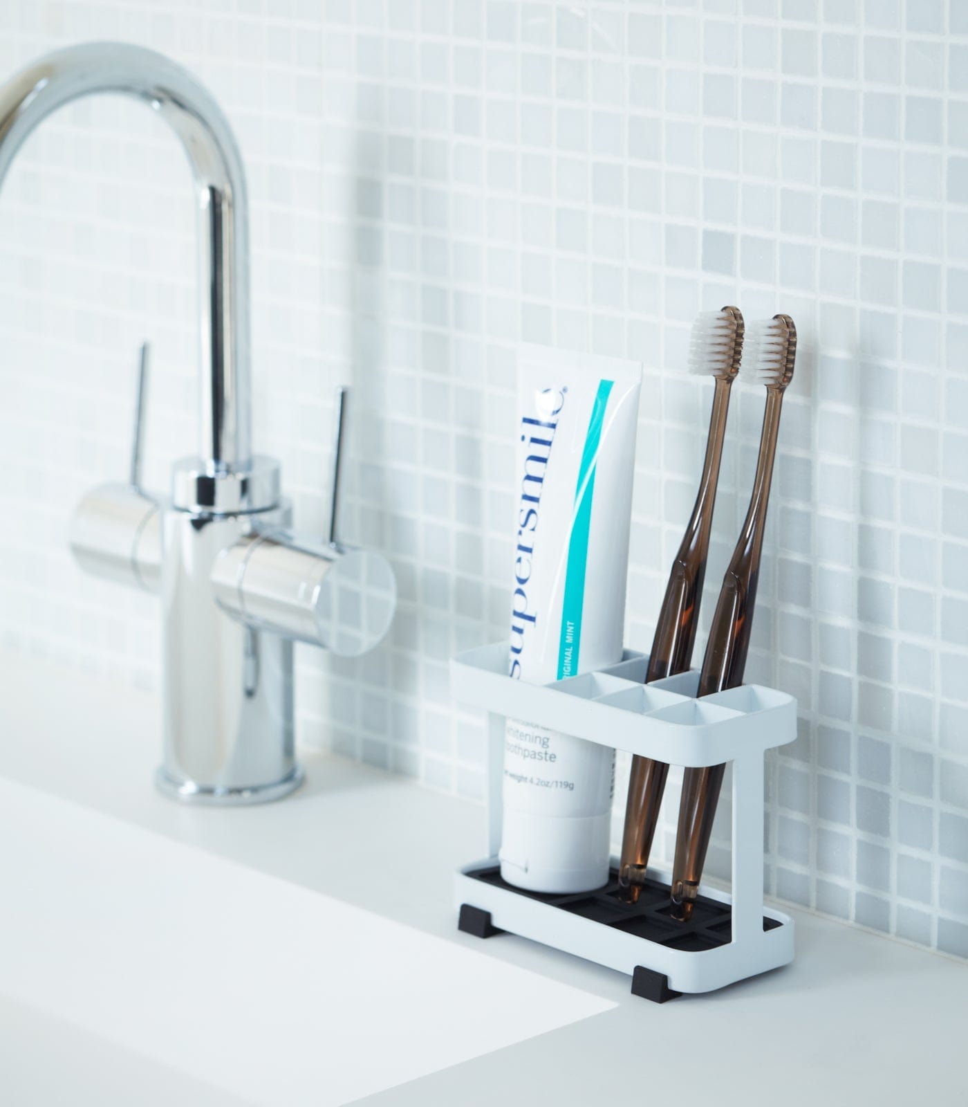 White toothbrush holder with toothbrushes and a bottle on a bathroom counter.