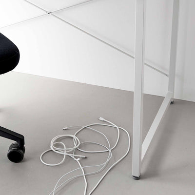 Loose white charging cables coiled on the grey floor beneath a white desk, illustrating the cable arrangement before using Yamazaki Home Magnetic Cable Holders With Adhesive Steel Bases (Set of 5) - Silicone.