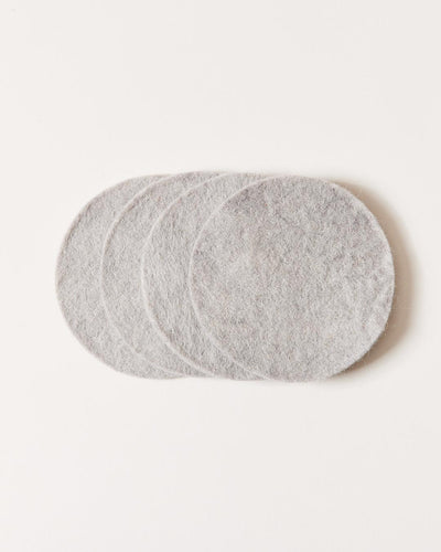 Stack of pale gray felt coasters arranged in an overlapping fan, showing their smooth circular shape and softly mottled fibers.