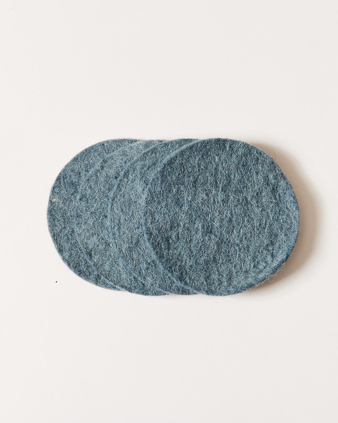 Stack of muted blue-gray felt coasters, slightly fanned to reveal their dense texture and rounded edges.