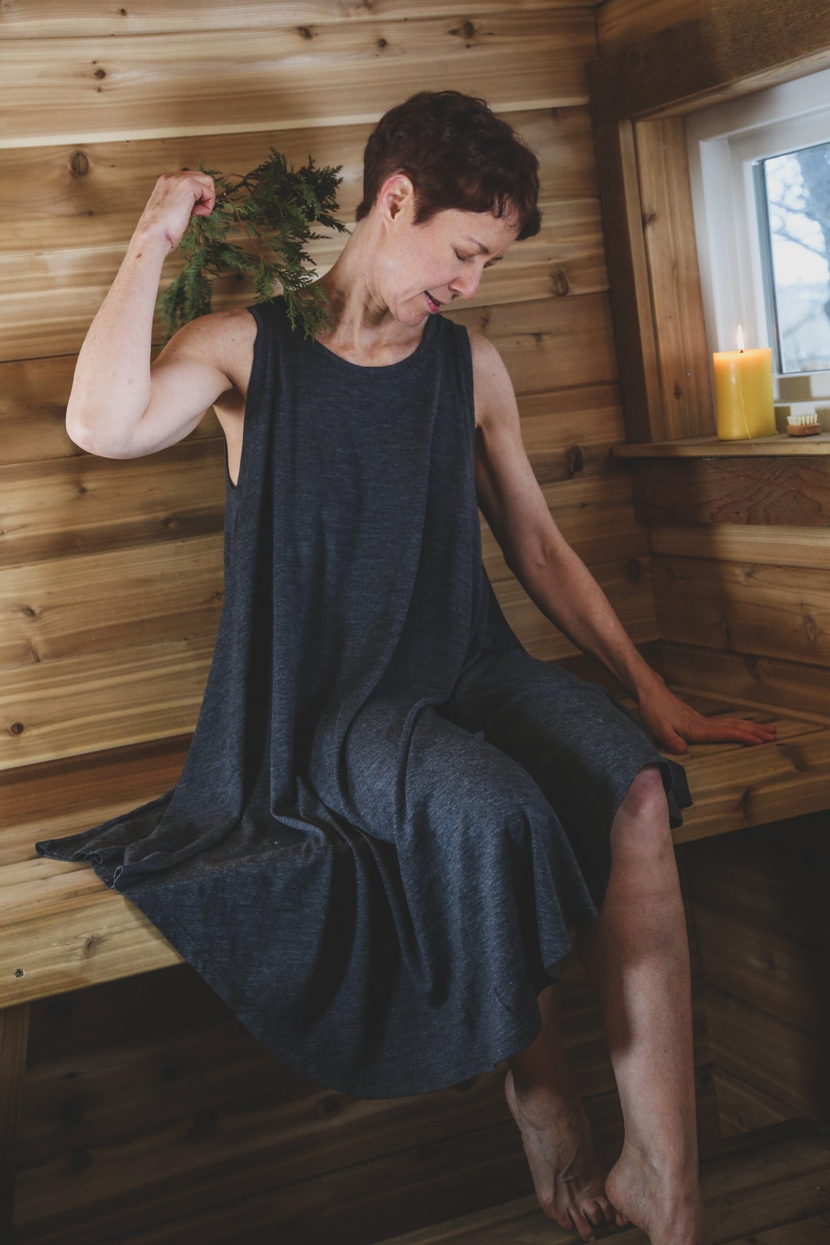 Woman wearing a charcoal merino wool sauna dress while seated in a Finnish sauna, designed for heat, cold plunge, and recovery.