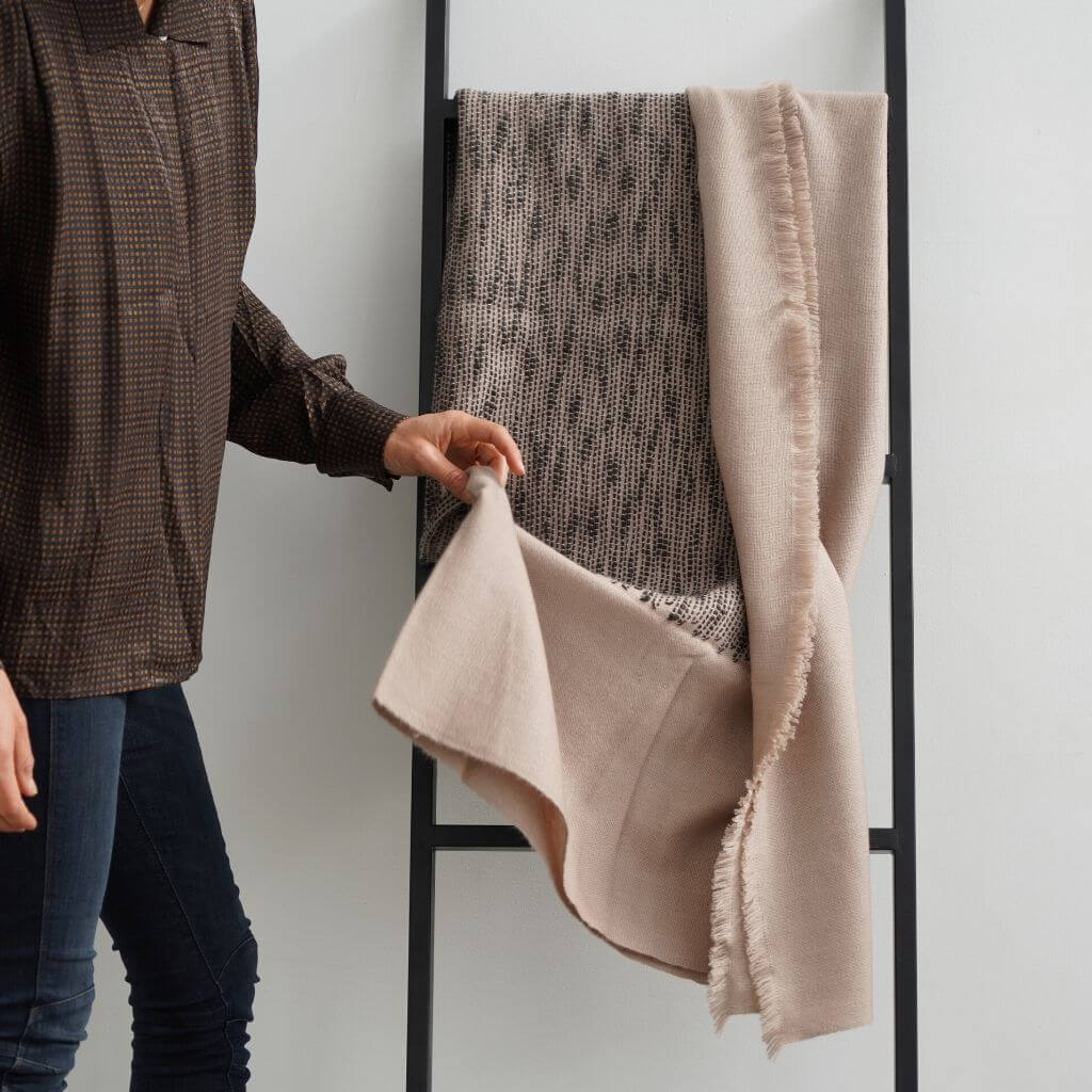 Person arranging the Flo Brown throw beside a black blanket ladder with coordinating neutral textiles
