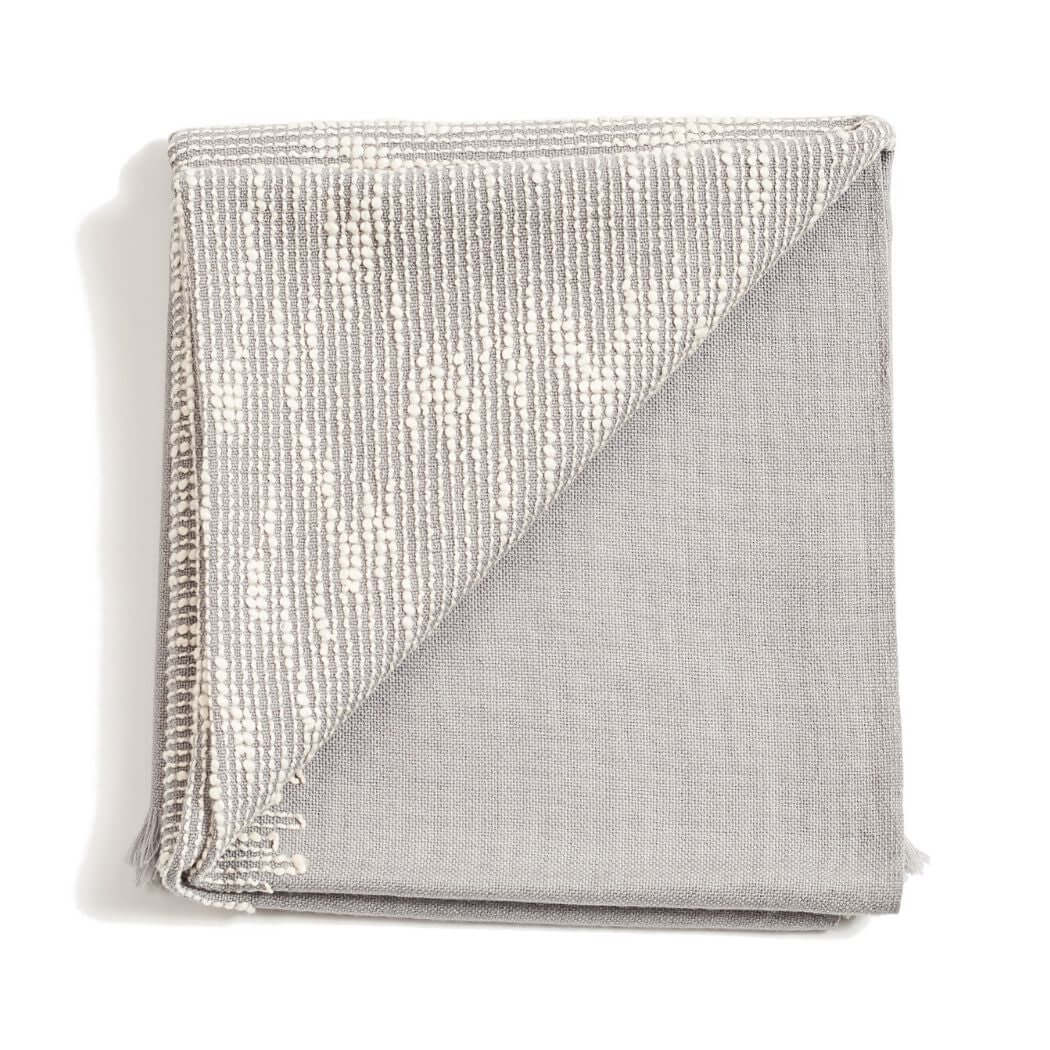 Folded gray color variation of the Variously Flo Handloom Merino Wool Throw with a pale textured pattern