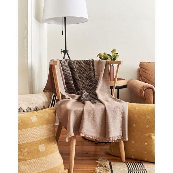 Flo Brown merino throw arranged over a wood chair in a warm living room with neutral furnishings