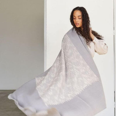 Woman holding the Flo Gray handloom throw open to display its full size, pale gray color and large white woven design