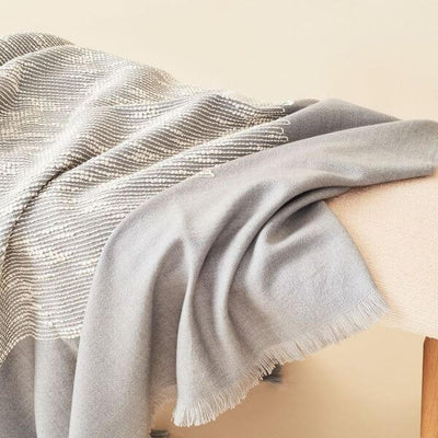 Close lifestyle view of the Flo Gray merino throw gathered over a beige seat with its fringe and woven texture visible