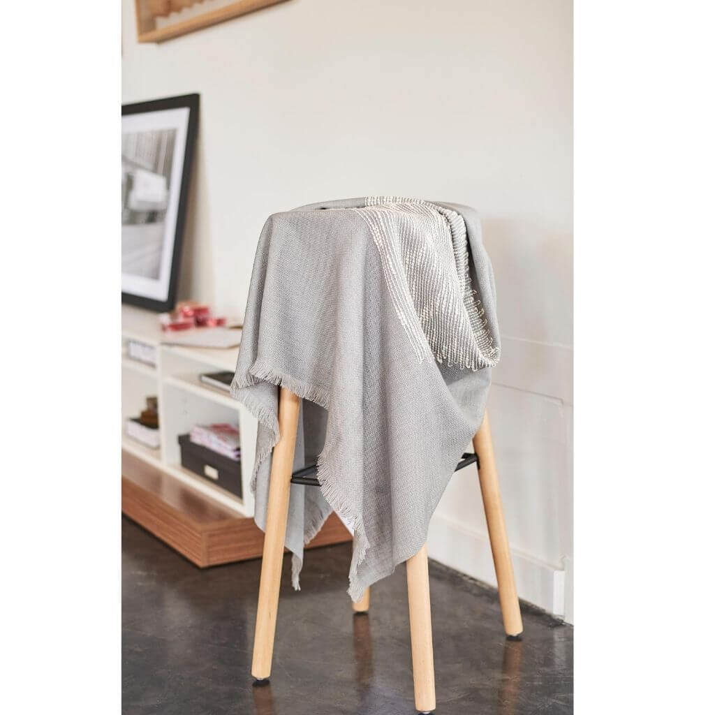 Flo Gray Textured Handloom Merino Throw draped over a tall wood stool in a modern room