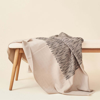 Neutral beige color variation of the Variously textured merino throw draped over a pale wood bench