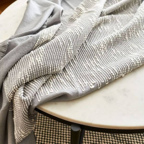 Flo Gray handloom throw loosely arranged across a round table, highlighting its contrasting weave and soft folds