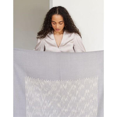 Woman holding the upper edge of the Flo Gray throw across her body to show the centered white textured pattern