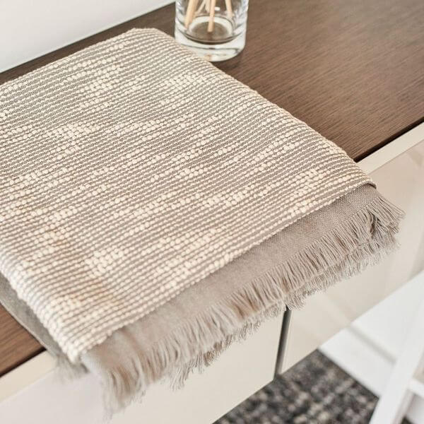 Folded Flo Gray handloom throw resting on a wood table, showing its dense white pattern and soft gray fringe