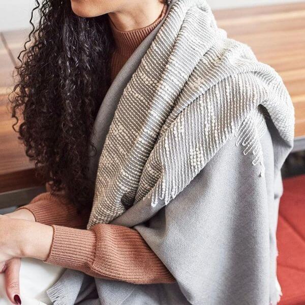 Woman wearing the Flo Gray merino throw around her shoulders, showing its soft drape and contrasting textured panel