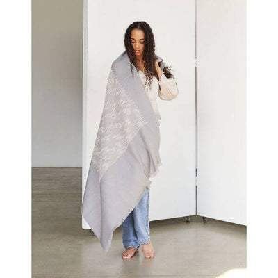 Full-length view of a woman wrapped in the Flo Gray merino throw with the pale textured design extending diagonally