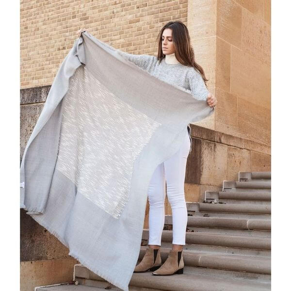 Woman standing outdoors and holding the Flo Gray merino throw fully open beside stone steps