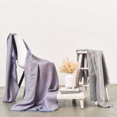 Flo Gray throw displayed with coordinating lavender and gray textiles draped over chairs in a minimalist setting