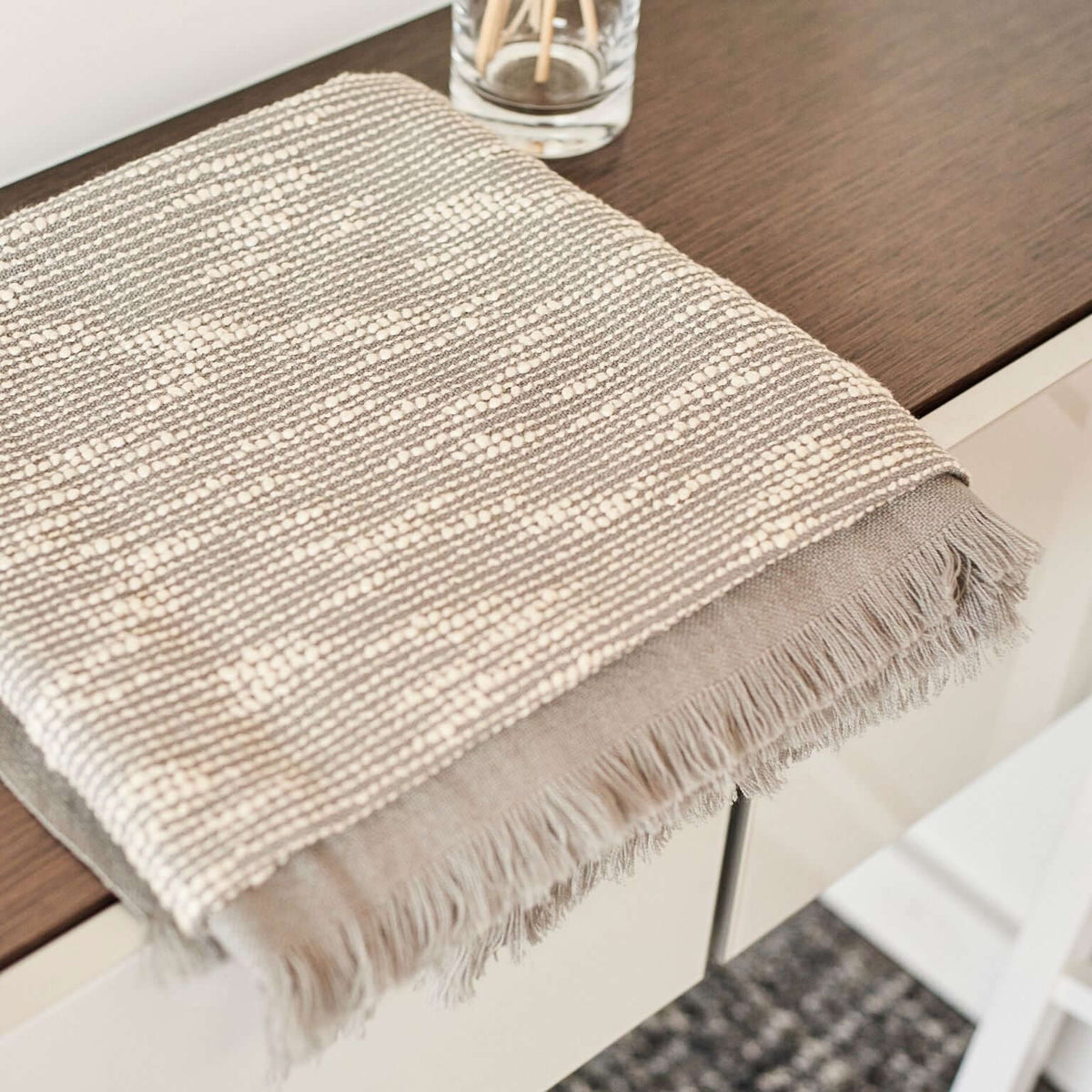 Close product view of the folded Flo Gray throw showing its woven white pattern and hand-finished fringe