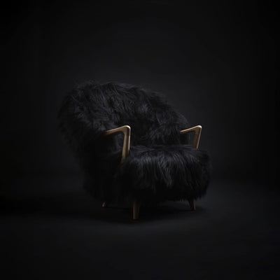 Eikund Fluffy Lounge Chair in a dim black studio, with directional light picking out the long black upholstery and curved light wood armrests.