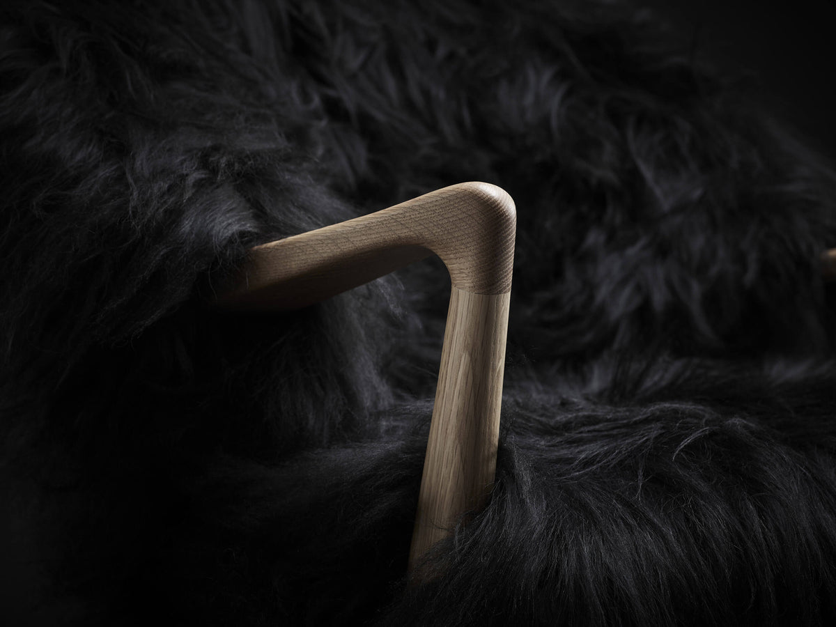 Close-up of the Eikund Fluffy Lounge Chair’s sculpted wood armrest, showing its rounded elbow-shaped joint and visible wood grain surrounded by long black upholstery.