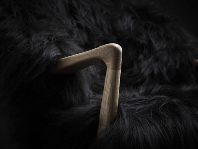 Close-up of the Eikund Fluffy Lounge Chair’s sculpted wood armrest, showing its rounded elbow-shaped joint and visible wood grain surrounded by long black upholstery.