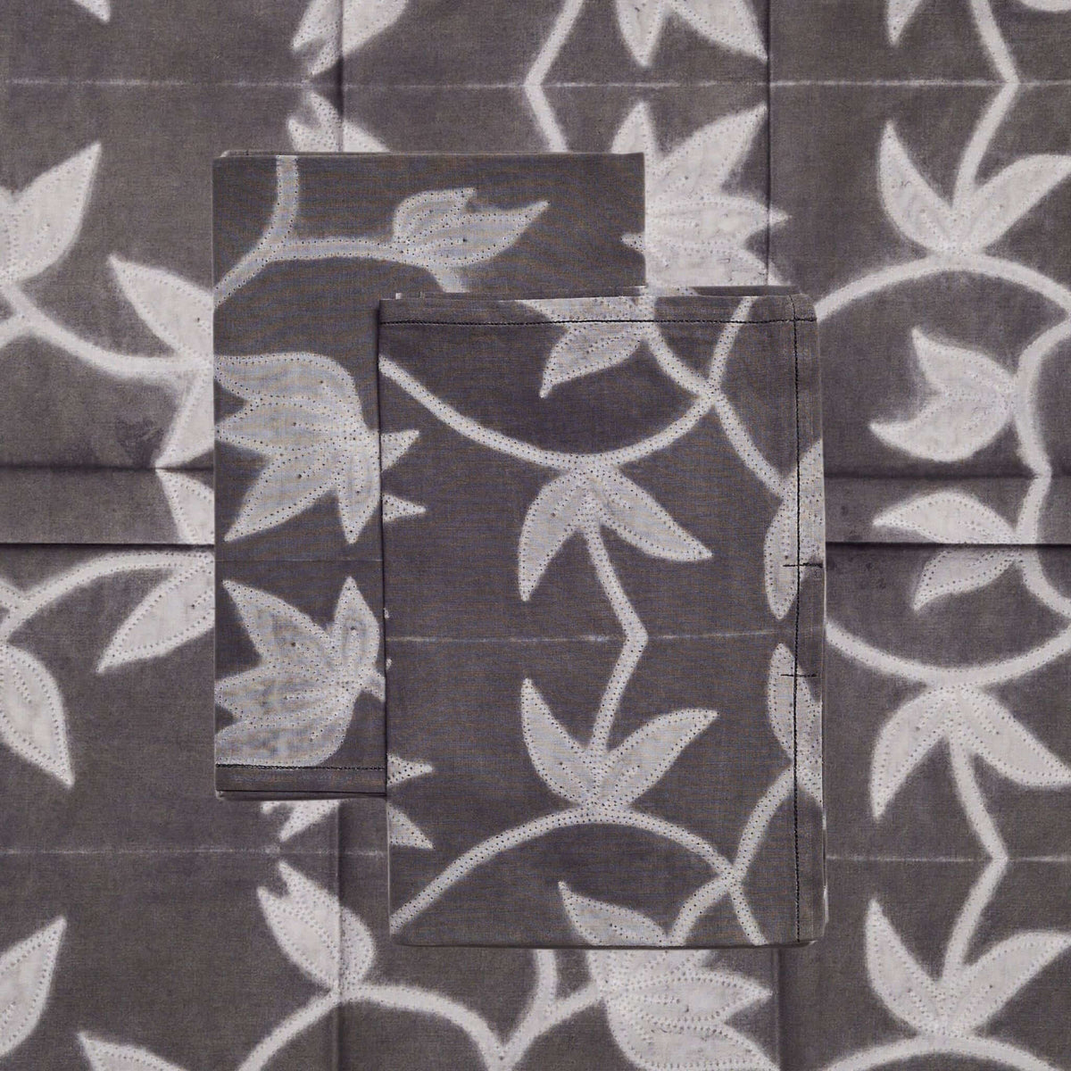 Close-up of the Folio Black napkin set showing pale gray leaves and winding stems across charcoal-black cotton