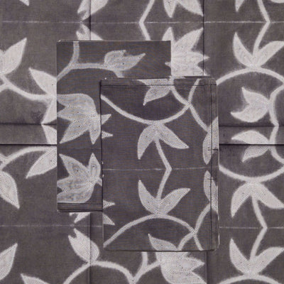 Close-up of the Folio Black napkin set showing pale gray leaves and winding stems across charcoal-black cotton