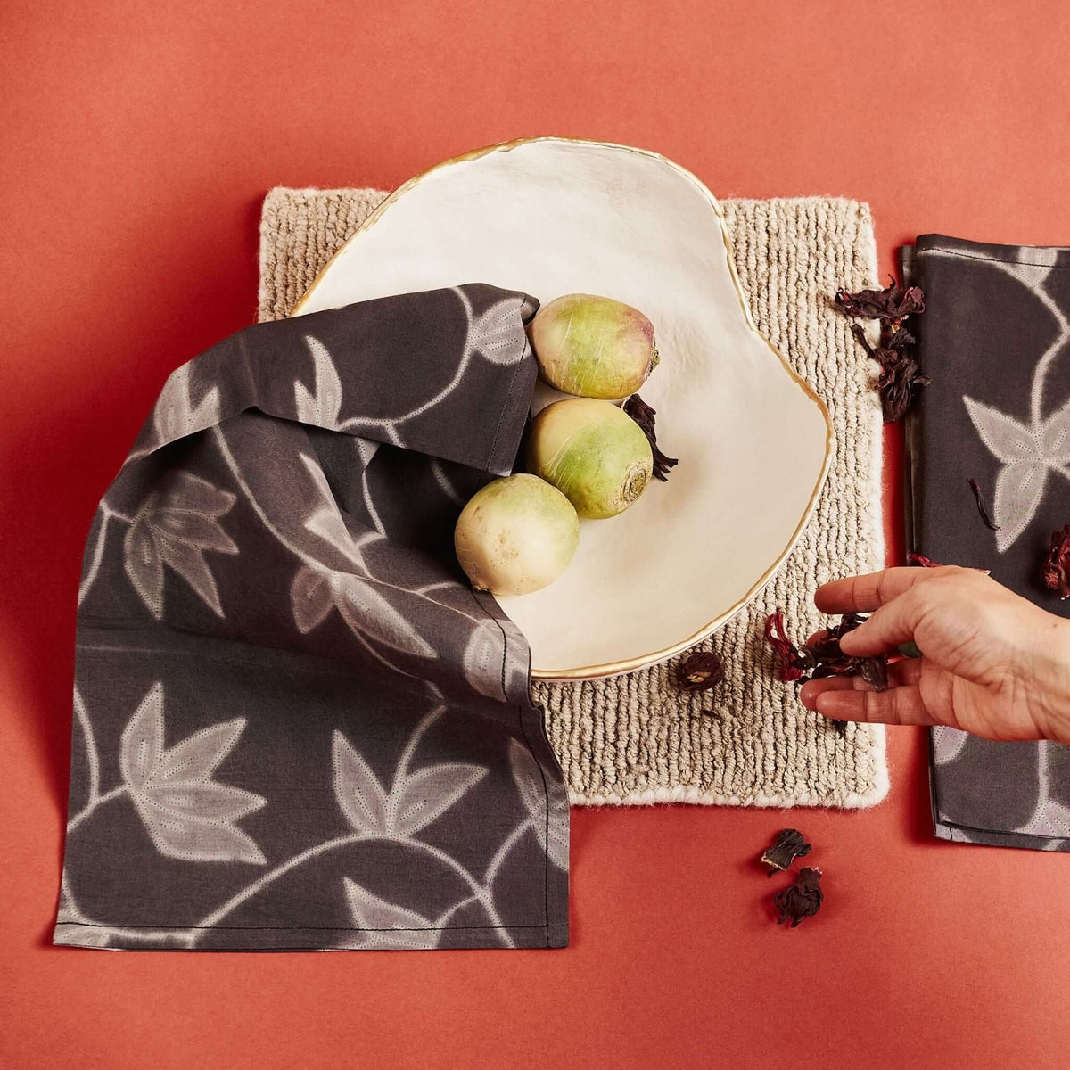 Variously Folio Black shibori cotton napkin styled beneath a white ceramic plate with green apples on a terracotta table