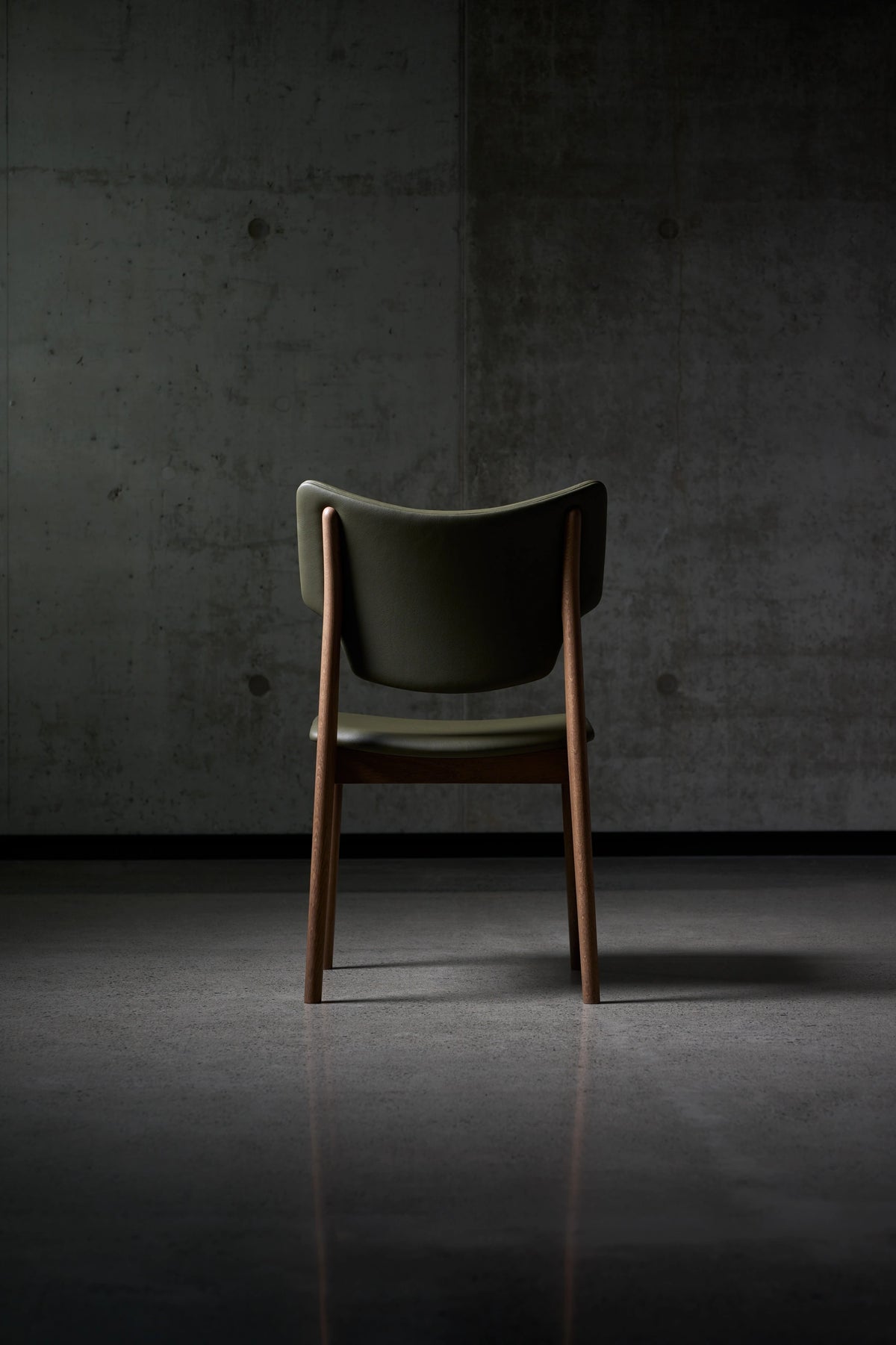 Rear view of the dark green Eikund Veng Dining Chair, showing the curved upholstered back between wood uprights above a dark tiled floor.