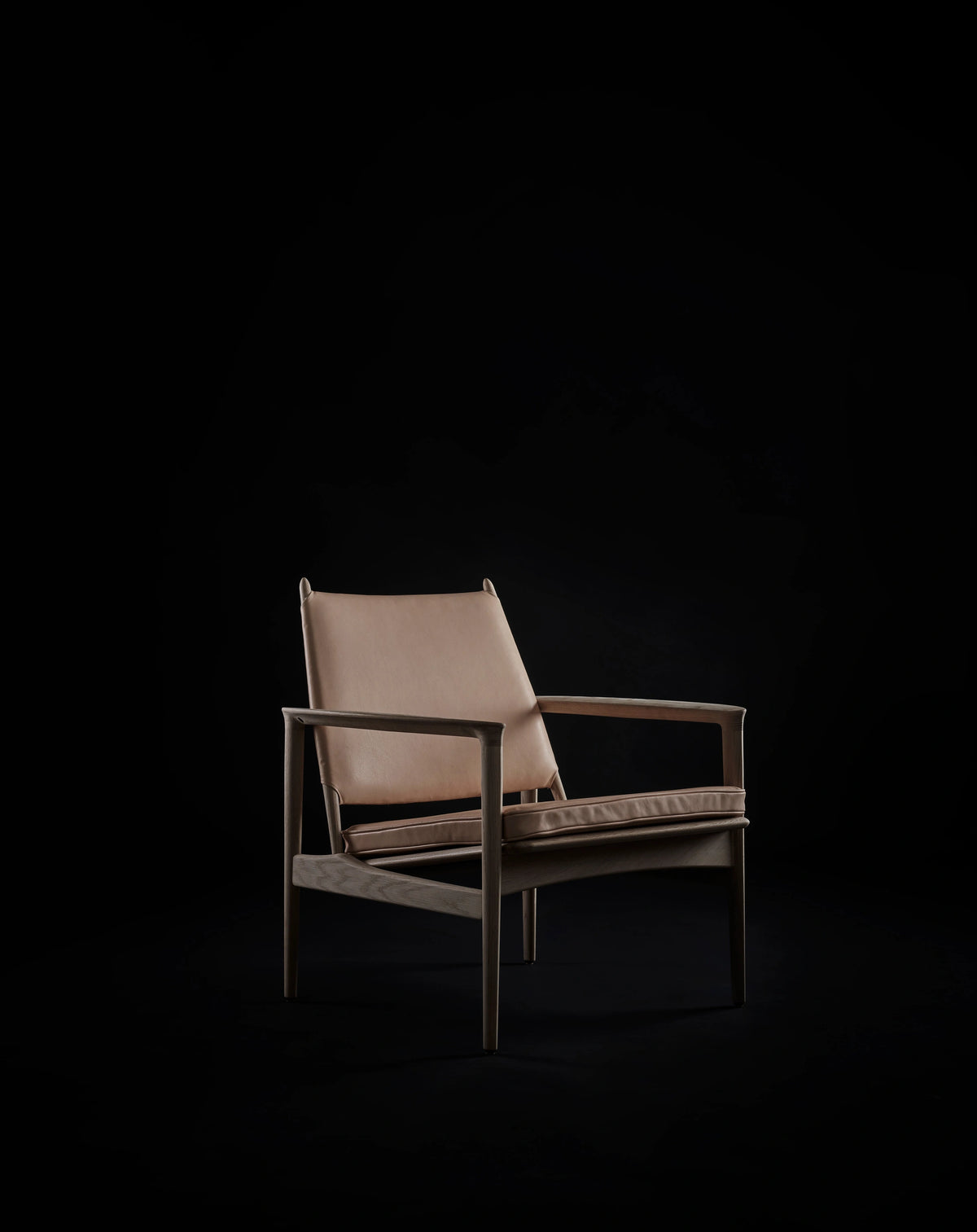 Pale tan leather Eikund Broadway Lounge Chair in a dark studio, showing the light upholstery, slim wood armrests, and open frame from a three-quarter front angle.