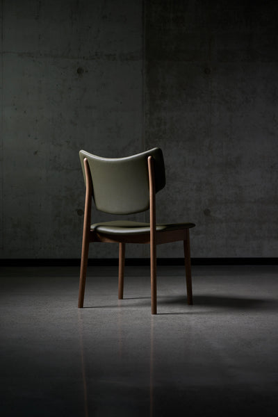 Three-quarter rear view of the dark green Eikund Veng Dining Chair, showing its curved back panel, exposed wood supports, and projecting seat.