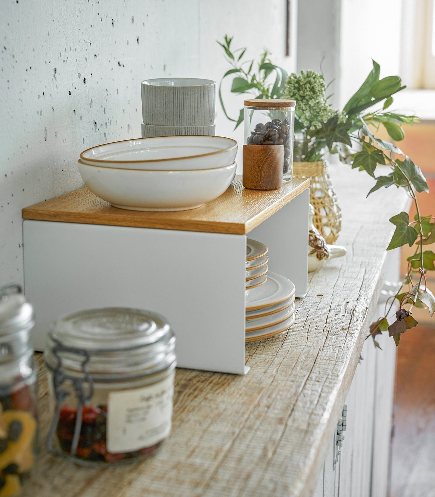 Kitchen counter with a white bowl, plates, and jars on a wooden surface.