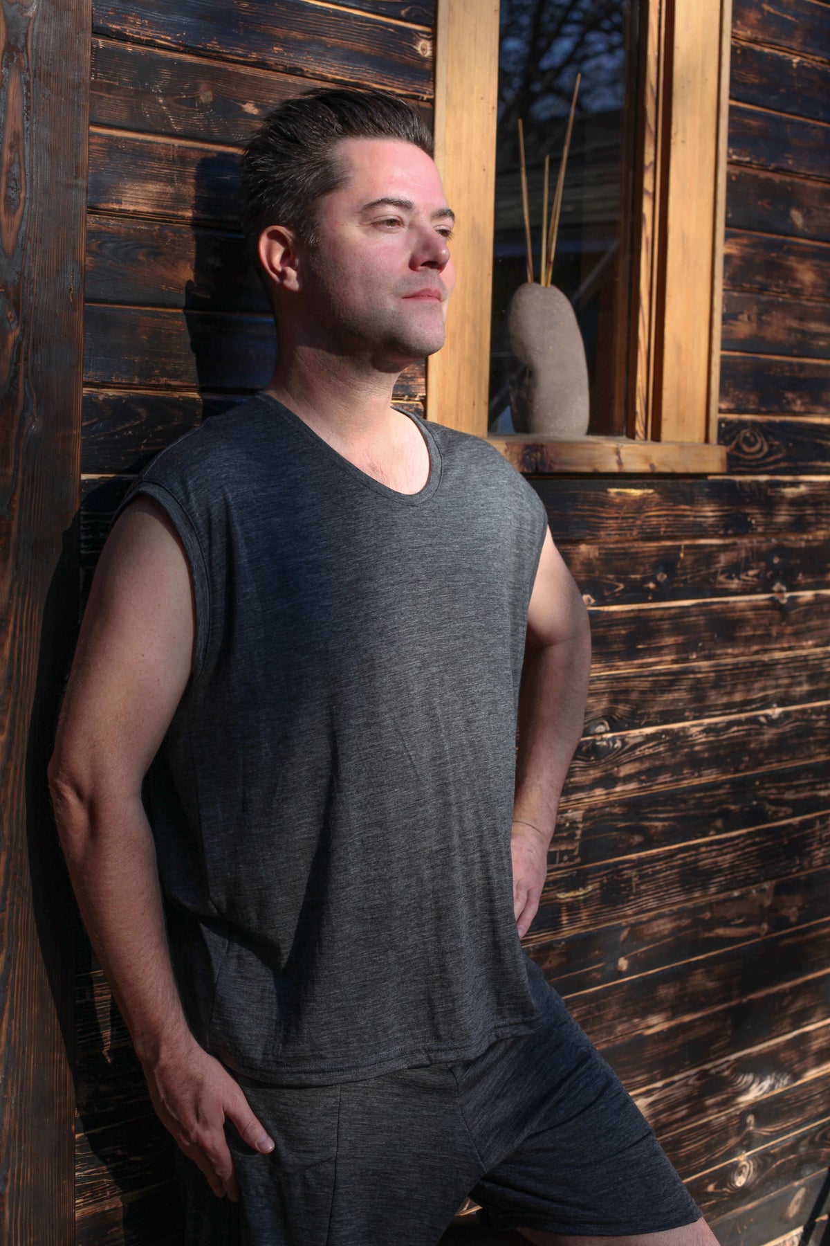 Man wearing a sleeveless merino wool sauna tee outside a sauna, designed for heat, recovery, and wellness rituals.