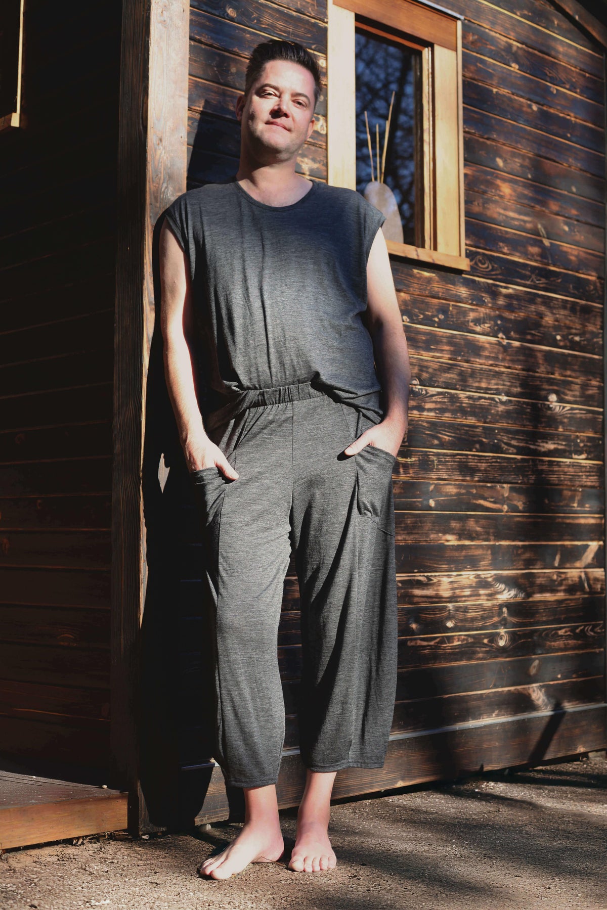 Full-length view of a man wearing a charcoal merino wool sauna tee and matching shorts designed for sauna and recovery rituals.