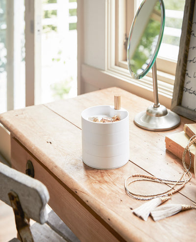Yamazaki Home Open Top Stacked Jewelry Organizer stacked into a white cylinder on a wooden dressing table, with jewellery in the open top tray beside a mirror and loose necklaces.