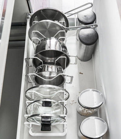 Overhead view of the white Yamazaki Home Adjustable Pot Lid Organizer - Steel in a drawer, showing cookware stored upright in individual slots with handles extending toward the back.