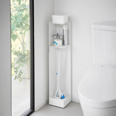 White Yamazaki Home Rolling Bathroom Organizer - Steel beside a toilet and window, with a tissue box on top, small bathroom supplies on the upper shelf and long cleaning tools in the lower compartment.