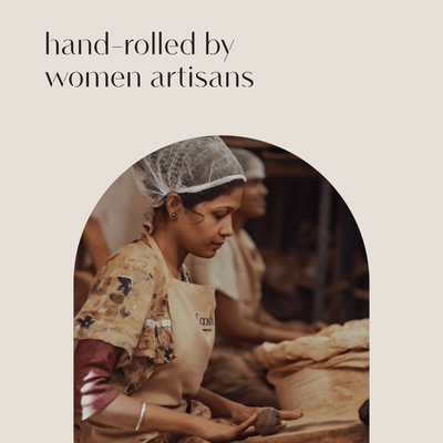 Woman artisan seated at a worktable hand-rolling Looshi incense sticks, framed beneath the words “hand-rolled by women artisans”
