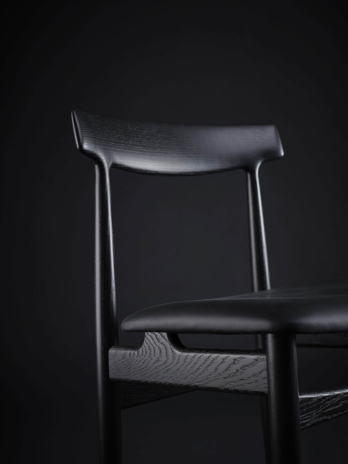 Close-up of the black Eikund Hertug Dining Chair’s upper frame, showing the sculpted backrest, narrow uprights, and visible wood grain on the rail beneath the seat.