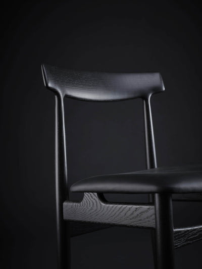 Close-up of the black Eikund Hertug Dining Chair’s upper frame, showing the sculpted backrest, narrow uprights, and visible wood grain on the rail beneath the seat.