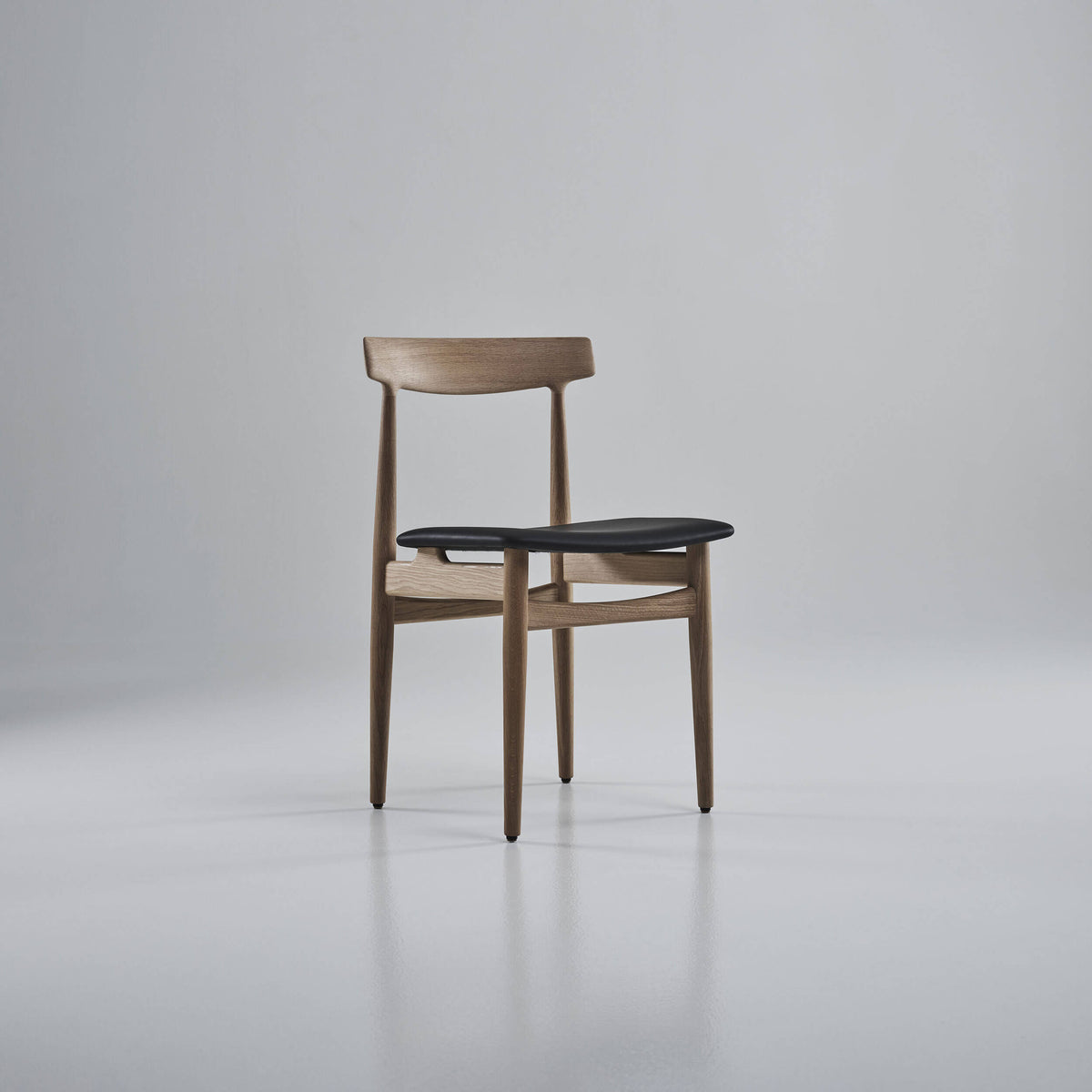 Three-quarter front view of the light wood Eikund Hertug Dining Chair with a black seat, showing the open back and curved rails beneath the seat.